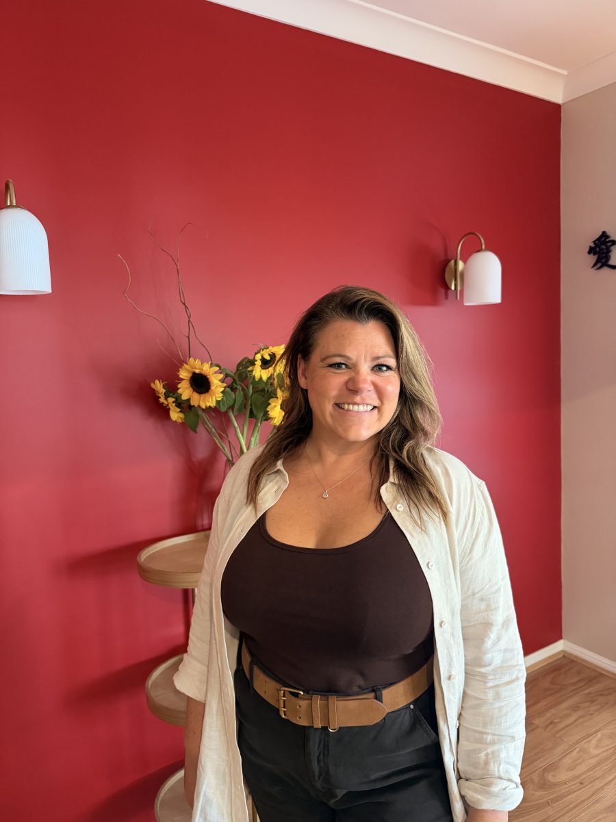 IMG_3620 A woman smiles before a red wall adorned with sunflowers and white wall lights in the background. Mornington Chinese Medicine